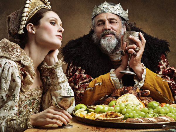 King, queen and feast with wine at table for fine dinning in royal banquet, vintage and majestic with crown. Monarch, husband and bored together with alcohol and buffet for formal celebration.