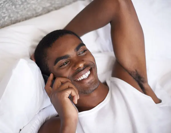 Happy, black man and bed with phone for communication, conversation or networking in relax at home. Face of African male person with smile on mobile smartphone for discussion in bedroom at the house.