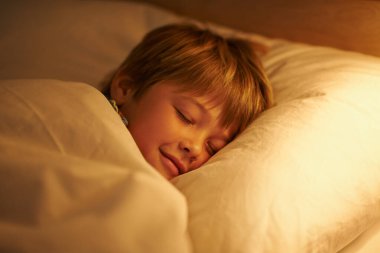 Oğlan, gece için yatak ve istirahat, yorgunluk ve huzur içinde uyumak. Çocuk, battaniyeyle, yastıkla, yatak odasıyla evde ya da evde huzurlu bir çocukluk için lambayla hayal kurar ve tükenir..