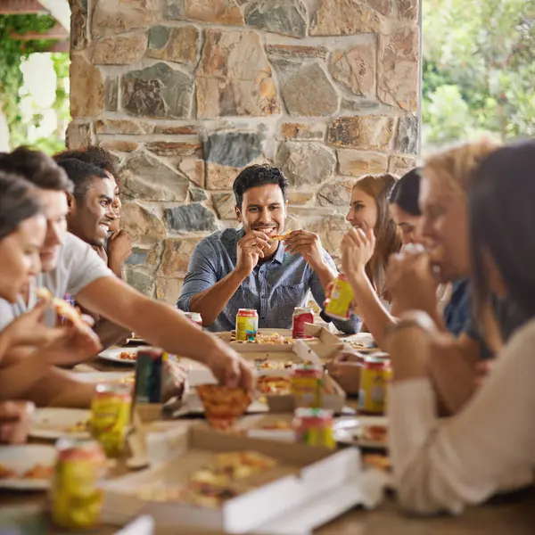 Friends, happiness and eating of pizza in home with talking, soda and social gathering for bonding in dining room. Men, women and fast food with smile, drinks or diversity at table in lounge of house.