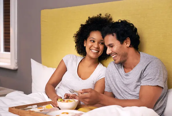 Couple, smile and bedroom for breakfast on tray for wakeup, morning and food for eat, rest and relax. Diverse and young people and laugh with happiness for bonding with fruit and bowl for joy.