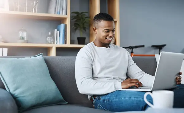 stock image Man, typing and laptop in home on sofa, networking and social media for online streaming in living room. Happy, research and technology on website, remote work and internet blog in apartment.