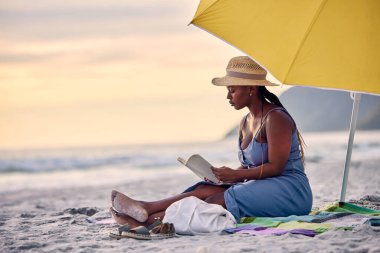 Gün batımı, dinlenme ya da yalnız kalmak, dinlenmek ya da tatil yapmak için deniz kenarında kitap okuyan siyahi kadın. Plaj, seyahat veya Yunan 'da bilgi, barış veya hobi için roman veya kurgu hikayesi olan Afrikalı kişi.