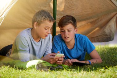 Çocuklar, kamp yapmak, sanal oyunlar oynamak ve tatil için çim üzerinde telefon ve çadır. Genç çocuklar ve cep telefonlarıyla konuşmak ve yaz tatilinde online eğlence ve maceraya meraklı olmak..