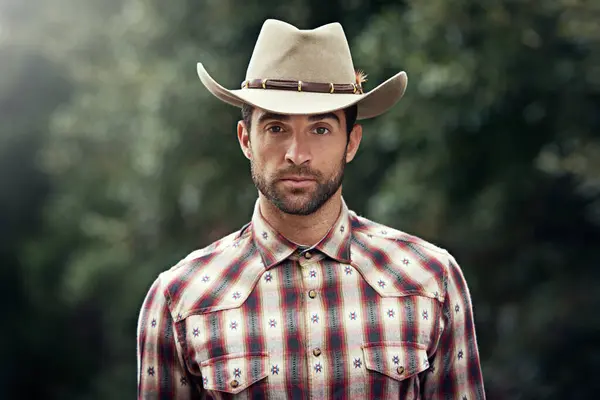 Man, portrait and outdoor cowboy clothes, western culture and countryside ranch in Texas. Male person, hat and flannel fashion for farmer aesthetic, nature and plaid style by trees or outside bush.