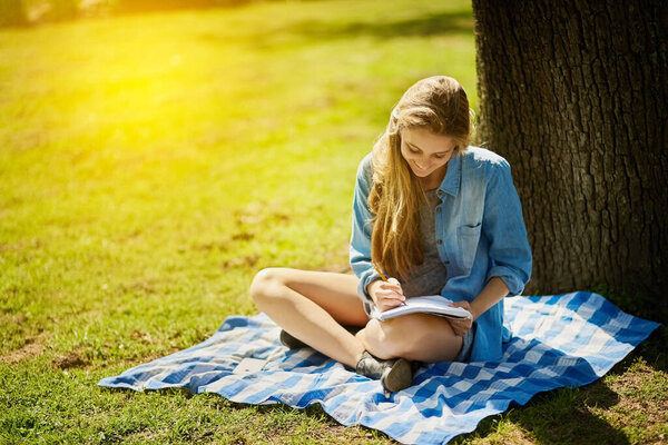 Young woman, happy and notebook for study in nature for test, education and scholarship in countryside. Female student, gen z and paper by tree for learning, reading and smile for brainstorming.