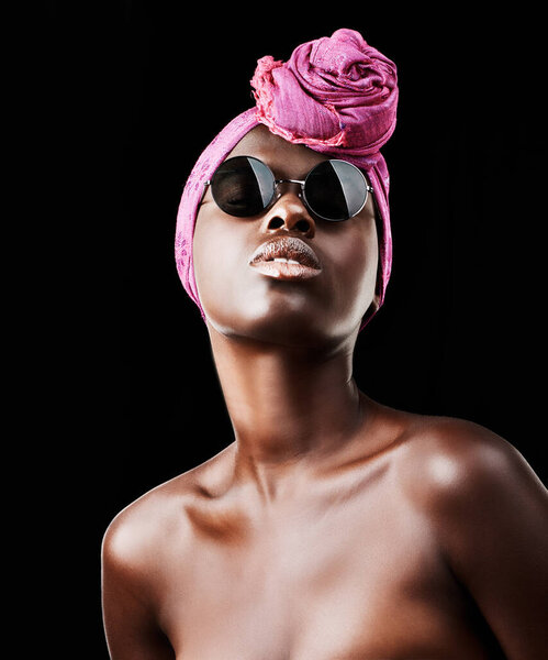 Face, fashion and culture with black woman in studio isolated on dark background for heritage. African, model and sunglasses with confident young person in trendy headwear for traditional style.