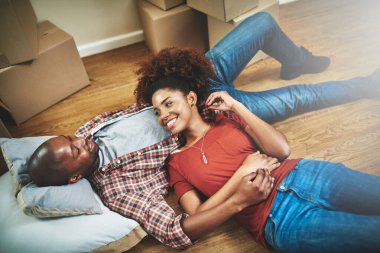 Siyahi bir çift, yeni evin zemininde kırılıp mutlu mesut oturuyor, destekliyor ya da üst açıdan rahatlıyor. İnsanlar, ev sahipleri ya da gayrimenkul yatırımları, hayallerindeki ev ya da gayrimenkul taşınması için heyecanlı kutular.