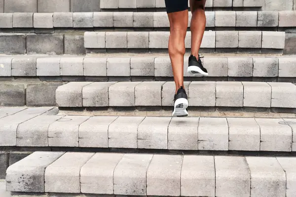 Athlete, legs and running up stairs in city for fitness, workout and exercise in summer. Runner, behind person and outdoor on steps for sport, wellness and cardio training for marathon in New York.
