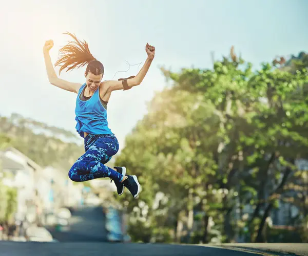 Woman, street and fitness with jump for celebration, speed and progress with training in summer. Girl, person or runner with cheers, winning and success for workout goals on road with achievement.