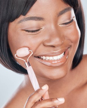 Skincare, derma roller and happy black woman in studio with wellness, cosmetics or anti aging treatment. Rolling skin, face and African beauty model with stone, crystal or lymphatic facial massage. clipart