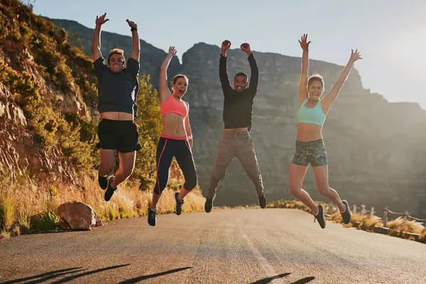 Road, fitness and jump to celebrate, friends and nature of mountain, portrait and happiness for wellness. Athlete, men and women in air, excited and exercise in summer, sports and outdoor together.