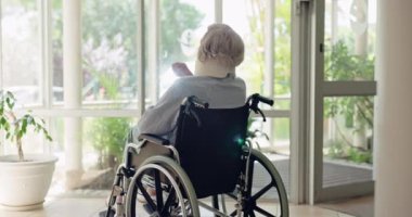 Yaşlı bir kadın, tekerlekli sandalye ve sabah güneşiyle pencerenin önünde iyileşmek için boyunluk takıyor. Kıdemli bayan, yaralanma ve rehabilitasyon için klinikte, hastanede ya da bakımevinde engelli olan kişi.