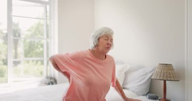 Yaşlı kadın, sırt ağrısı ve huzurevinde artrit, yatak odası ve sağlık sorunları. Yaşlı kişi, osteoartrit ve evde yaralı, stresli ve hasta yatağında yatıyor..