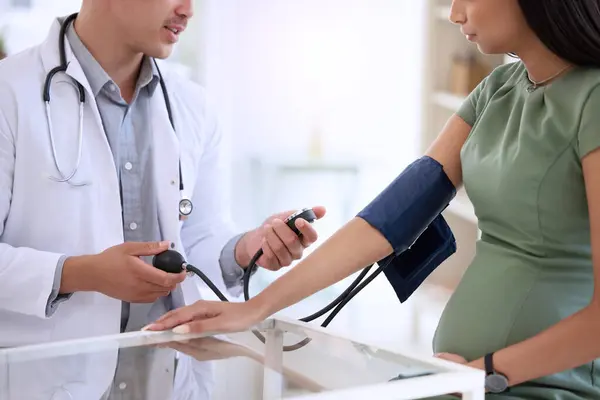 stock image Doctor, man and pregnant woman in hospital for blood pressure, healthcare checkup and consultation. Male medical expert, pregnancy and patient with hypertension by desk for preeclampsia and wellness.