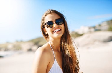 Portrait, beach and woman with sunglasses, excited and smile with happiness, holiday and weekend break. Face, person and girl with eyewear, seaside and vacation with getaway trip, travel and sunshine.