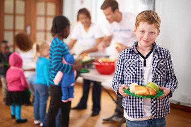 Boy, food and charity in portrait at shelter, soup kitchen and happy for kindness, care and volunteer services. Kid, plate and smile for meal, nutrition and gratitude for donation from church group.