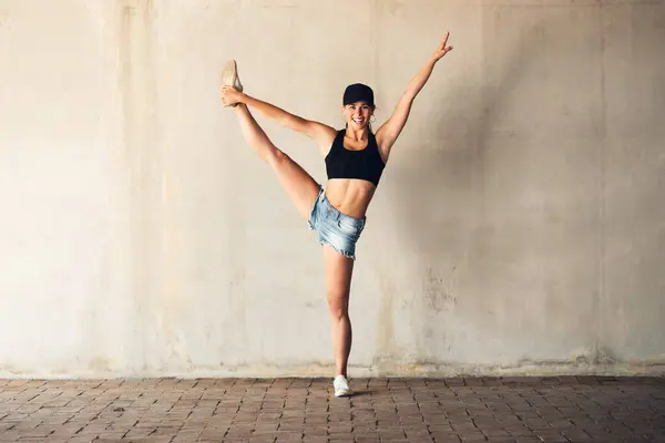Girl, street dancer and hip hop in city with balance, steps and lift leg in portrait at training. Woman, person and dancing for culture, art and stretching with rhythm for performance on sidewalk.