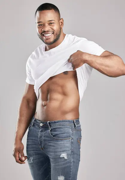 Jeans, muscle and black man with portrait, smile and tshirt for abs, fitness and wellness in studio. Workout, healthy and African person with fashion, clothes and model, strong and white background.