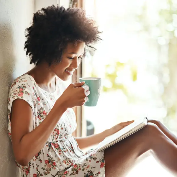 stock image Woman, reading and book in home with coffee, door way and sitting on floor for comfort with literature or novel for hobby. Fiction, fantasy and knowledge or information, apartment and relax weekend.