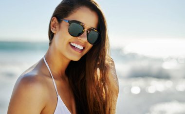 Portrait, beach and woman with sunglasses, smile and sunshine with happiness, tropical island and weekend break. Face, person and girl with eyewear, seaside and holiday with getaway trip and travel.