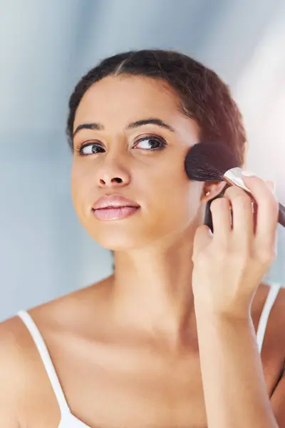 stock image Beauty, makeup brush and black woman on cheek in bathroom for cosmetics, grooming or foundation. Powder, hand and female person with tools for applying contour, glowing skin or getting ready in home.