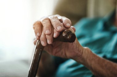 Senior man, hands and walking stick with cane for support, old age or care in retirement home. Closeup of elderly, pensioner or male person with a disability for stability, assist or posture at house.