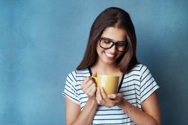 Stüdyoda gülümseyen, içen ve mavi arka planda gözlüklü bir kadın, öğrenci ve kahve. Modifiye et, kafein ve enerji veya öğrenci, el ve kibrit veya susuzluk için yeşil çay ve rahatlama için sağlık.