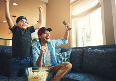 Televizyon, çocuk ve erkek kanepede birlikte maç izleyip, yayın yapmak için başarılı olacaklar. Evlat, baba ve televizyon kumandalı patlamış mısır. Kutlama, kaynaşma ve canlı yayın için..