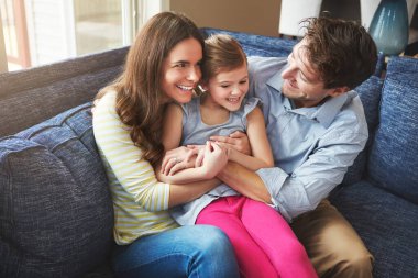 Gıdıklanıyor, gülüyor ve anne babasıyla evdeki kanepede oturup birlikte eğleniyor, eğleniyor ve sevişiyorlar. Mutlu, bağlanan ve aile evinde anne ve babasıyla oynayan kız çocuğu.