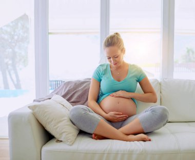 Rahatlamak, gülümsemek ve hamile bir kadının evde karnını tutup mutlulukla doğum bakımı yapması. Avustralya 'dan gelen midesi olan sevgi, dinlenme ve anne gibi bir kadın dairede oturuyor.
