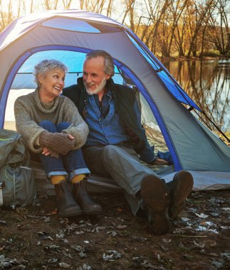 Yaşlı çift, çadır ve doğa ile kamp, dinlenme ve emeklilik ile tatil, kaçış veya mola. Açık havada, güneşli, dağlı ya da tatilli yaşlı erkek ya da olgun kadın sohbet ederek ya da dinlenerek..