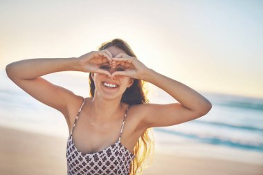 Kadın, portre ve kalp plajda gözlerinde sevgi, şefkat ya da deniz şefkatinin işareti olarak bir gülümseme ile. Kız, mutlu ve seçim simgesi ile tatil, gün batımında konum için dalgalar tarafından geri bildirim gibi.