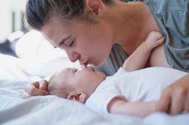 Anne, bebek ve evde destek, sevgi ve çocuk gelişimi için yatakta öpücükle mutlu. Ebeveyn, çocuk ve yatak odasında, bağ kurmak, çocukluk anıları ve yeni yürümeye başlayan çocuk için oynamakla mutlu..