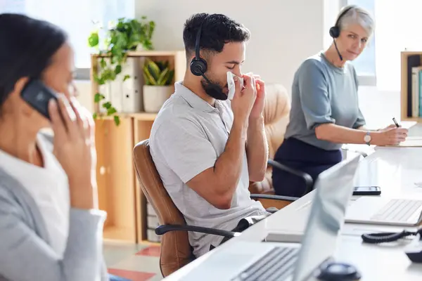 stock image Man, blowing nose and call centre office for business, employee and sick in coworker workspace. Allergy, customer care and technical support agent or immune virus, telecom salesman and health risk.