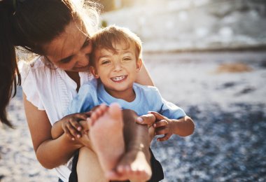 Anne, çocuk ve plaj neşeyle gülüyor, deniz kenarında sarılıyor ve gülüyor sevgi, özen ve bağlılık ile. Tatil, tatil ve ebeveynler ve oğlanla birlikte açık hava seyahati. Yazla ve seyahatle birlikte okyanus kenarında..