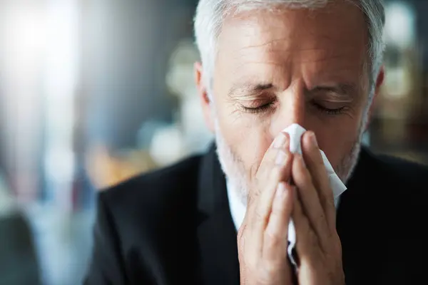stock image Business, blowing nose and man with tissue, bacteria and disease with burnout, sick and cold in workplace. Mature person, agent and lawyer with allergy, overworked and sneeze with flu season.