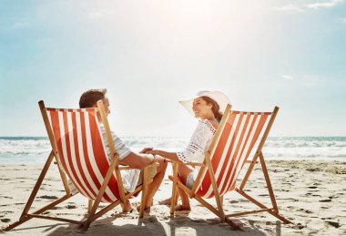 Çiftler, tatil macerası için plaj sandalyesinde rahatlayın. Yaz yolculuğunda eşinizi sevin ve destekleyin. Mutlu, kadın ve erkek okyanus özgürlüğü, güven ve Bali adasında el ele tutuşuyorlar..