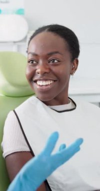 Randevu, gülümseme ve dişçi muayenesi için dişçiyle konuşan siyah bir kadın. Sağlık hizmetleri, ağız sağlığı ve danışmanlık veya diş temizliği için sandalyeye oturan hasta.