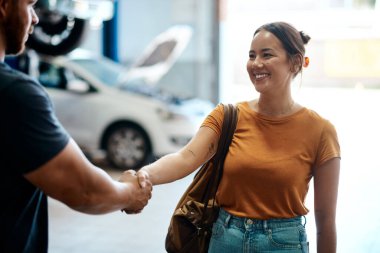 El sıkışma, gülümseme ve tamirci ile birlikte tamirat ya da tamirat için çalışan bir kadın. Happy, anlaşma ve Asyalı kadın araba servisi için garajda endüstriyel işçiyle tokalaşıyor..