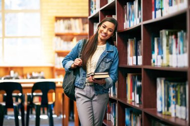 Kadın, portre ve öğrenci kütüphanede kitap, mutlu ve akademi edebiyatı veya üniversite tezi ile kampüste. Burs, atama ve kitaplık için eğitim, bilgi ve üniversite bilgileri.