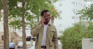 Mutlu, siyah bir adam ve iletişim ya da açık hava sohbeti için şehirde telefonla yürüyor. Şehirdeki dostça bir tartışma için cep telefonuyla gülümseyen Afrikalı erkek..