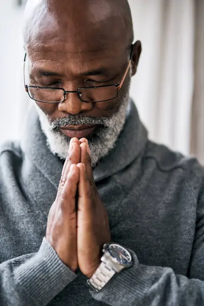 Stock image Praying, hands and elderly black man in house with peace, gratitude and grace, mercy or trust in God. Worship, spirituality and calm senior African person with thank you prayer for Jesus Christ.