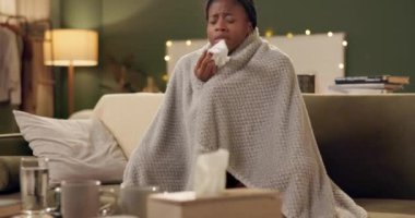 Kadın, hasta ve kanepede battaniyeyle hapşırıyor burnunu silmek, iyileşmek ya da kış virüsünü salona yaymak için. Afrikalı, enfeksiyon kapmış, ateşi, sinüsü ya da alerjisi olan biri..