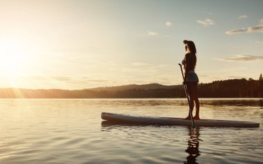 Göl, güneş ışığı ve ağaçlı kürek çeken kadın, su sporu ve turizm için nehirde tatil. Almanya 'da kadınlar için egzersiz, gündoğumu veya tatil, macera için manzara ve seyahat uygunluğu.