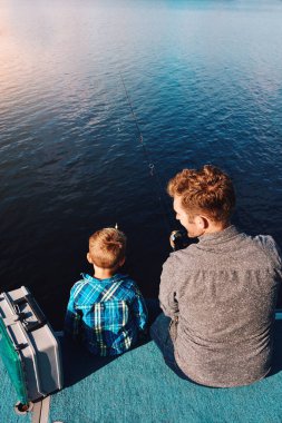 Yukarıda, çocuk ve baba gölde balık tutmak, yaz ve tatil için gün ışığı öğretiyorlar. Aile, balıkçı ve çocuk doğada tatil, öğrenme ve babamla açık hava macerası için su kenarında..