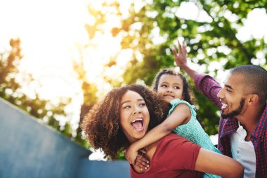 Mutlu aile, sırtında taşıma ve kızıyla doğada oynaşma özgürlüğü veya açık hava eğlencesi için. Baba, anne ve çocuk ya da tatil için gün ışığında gülümseyen küçük kız ya da arka bahçede sarılan..