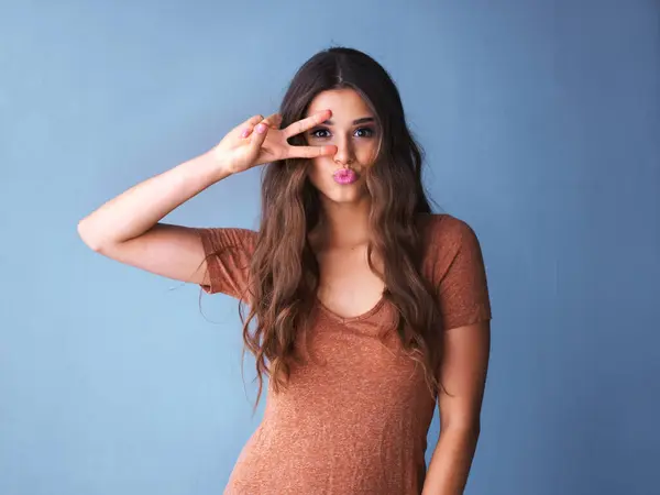 stock image Portrait, hand and woman with peace sign in studio for happiness, good mood or face expression on blue background. V, emoji and female model with kiss for gesture, positive attitude or symbol.