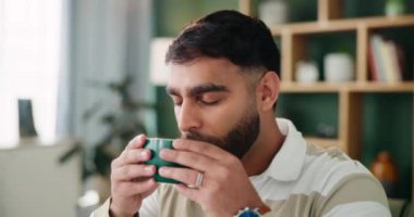 Indian man, couch and drinking coffee in home for peace, espresso and beverage on weekend. Male person, relax and taste of matcha for comfort in lounge, thinking and camomile to rest in apartment.