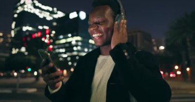 Siyahi bir adam, açık havada müzik listesi için kulaklıkla akıllı telefonda dans ediyor, gece New York 'ta eğleniyor. Şarkılı ve videolu yayın platformu için mutlu ve internetteki kadın.